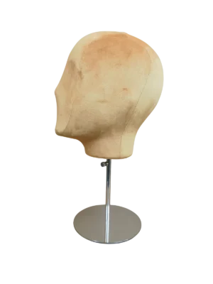 Vista lateral de una cabeza de maniquí abstracta XINTU, cubierta de terciopelo beige, sobre un soporte ajustable de metal plateado con base redonda.