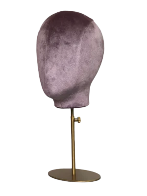 Vista en ángulo de una cabeza de maniquí abstracta XINTU, tapizada en terciopelo rosa púrpura, sobre un soporte metálico redondo dorado ajustable.
