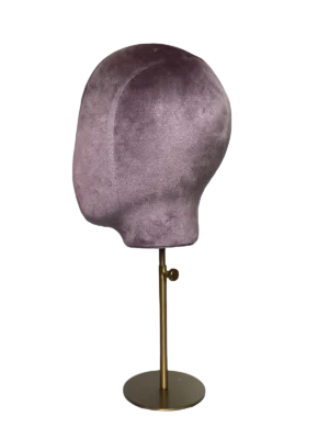 Perfil lateral de una cabeza de maniquí abstracta XINTU, tapizada en terciopelo rosa púrpura, sobre un soporte redondo de metal dorado.