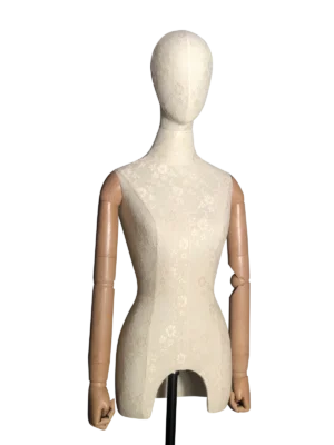 Vista en ángulo del torso de un maniquí femenino XINTU, cubierto de tela de encaje blanca, con una cabeza abstracta y brazos articulados de madera.