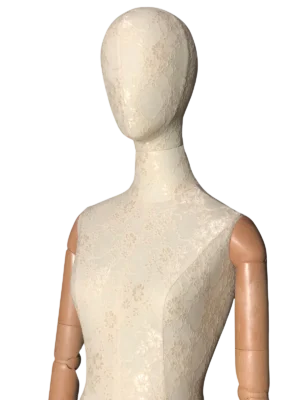 Primer plano frontal del torso de un maniquí femenino XINTU, cubierto de tela de encaje blanca, con una cabeza abstracta y brazos articulados de madera.