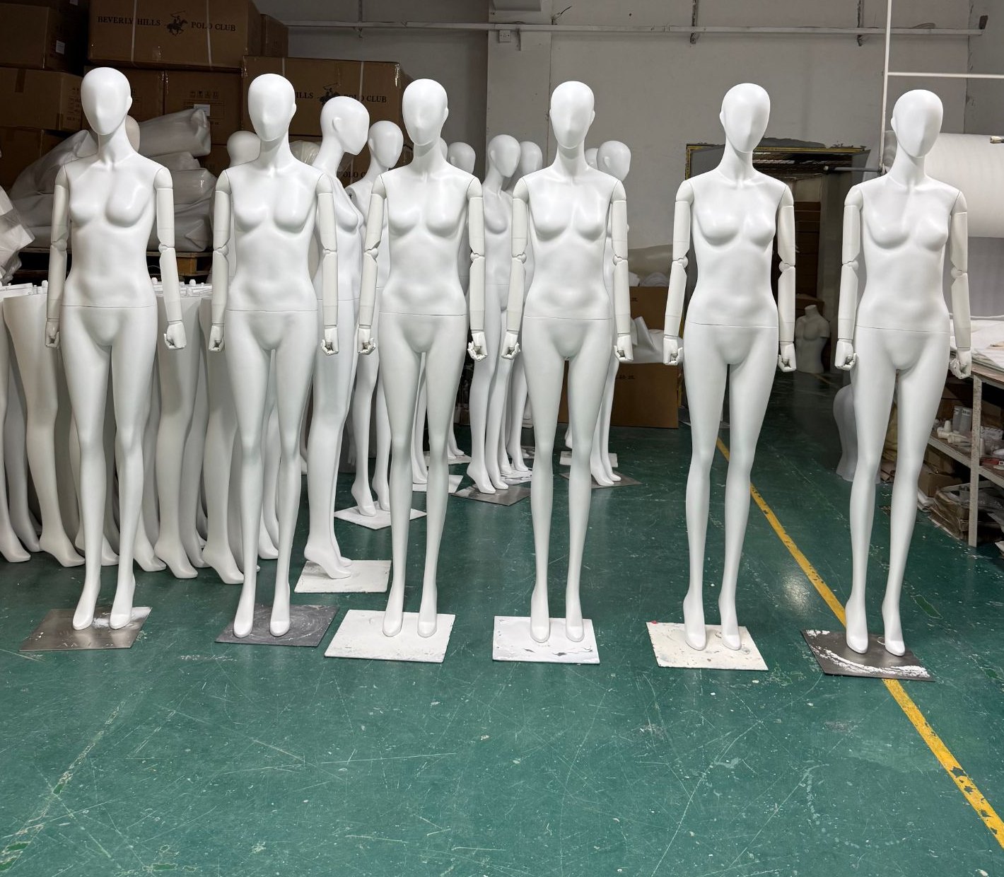 Six white fiberglass full-body female mannequins with square metal bases in a factory